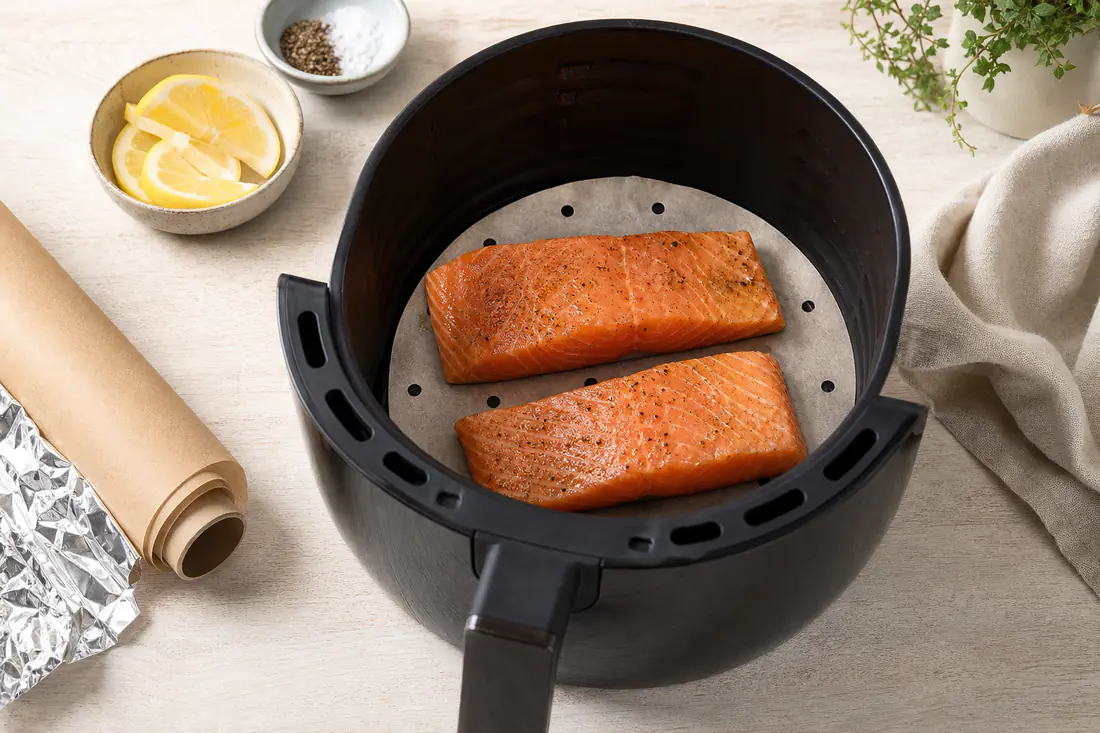 Perforated baking paper liner fitted in an air fryer basket with fish fingers on top