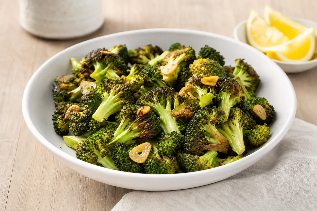 Roasted broccoli florets with crisp browned edges and lemon wedges in a white bowl