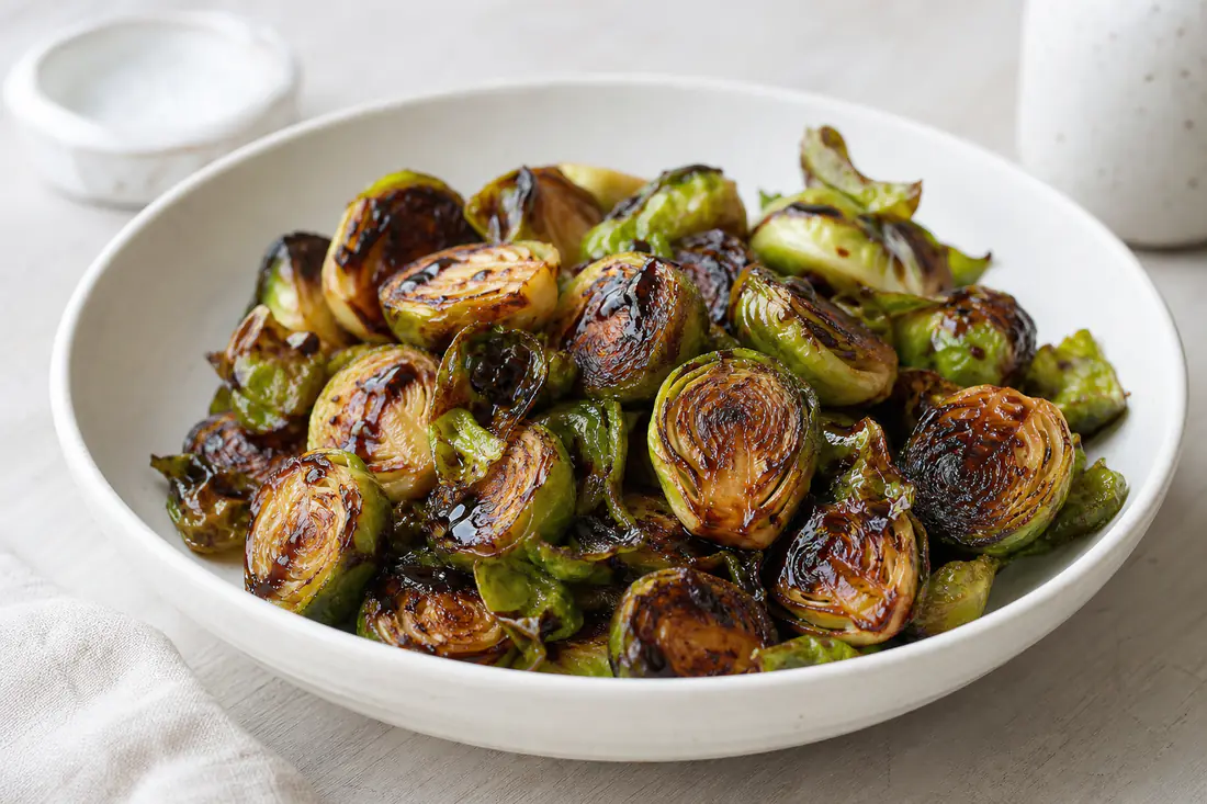 Halved Brussels sprouts with crisp caramelised edges and a drizzle of balsamic glaze in a white bowl