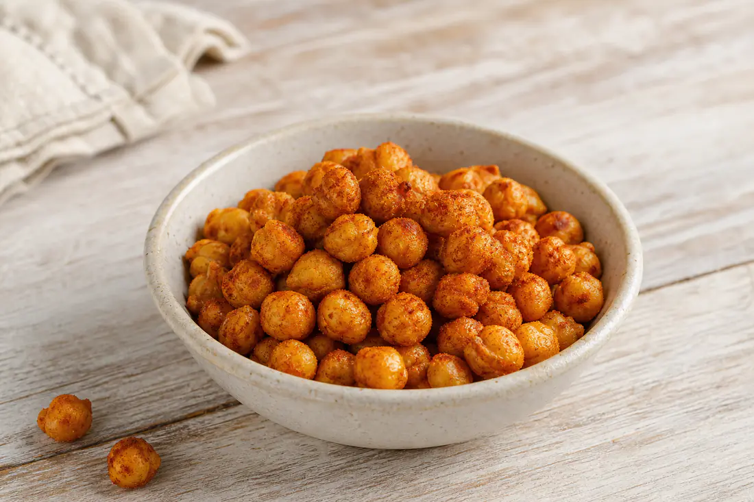 A small bowl of golden crispy roasted chickpeas dusted with paprika on a wooden table
