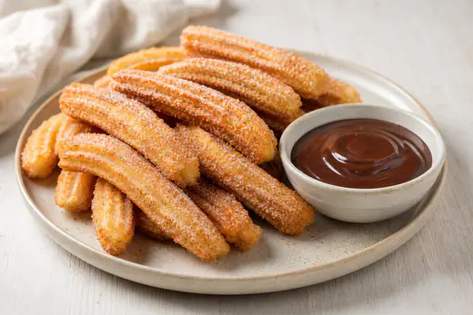 Ridged golden churros rolled in cinnamon sugar beside a small bowl of chocolate dipping sauce