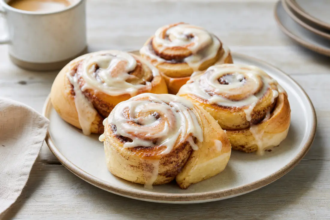 Soft cinnamon rolls with cream cheese icing on a plate next to a cup of coffee
