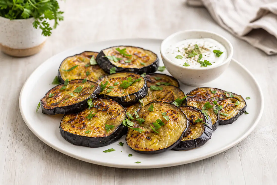 Golden roasted aubergine slices with crisp edges, parsley and yoghurt dip on a white plate