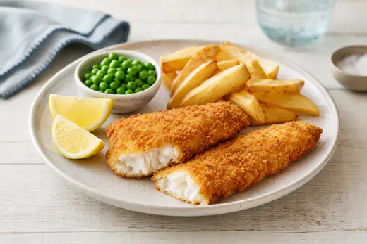 Two crisp golden breaded fish fillets and a few chips on a plate with lemon wedges and peas