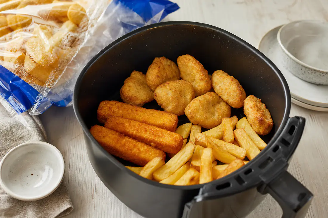 Golden frozen chips, fish fingers and chicken nuggets cooked in an air fryer basket