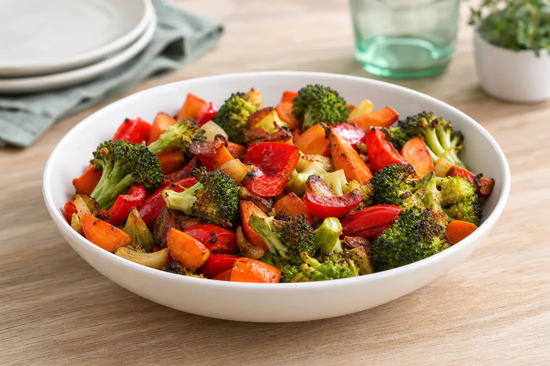 Roasted mixed vegetables with broccoli, carrots and peppers in a white bowl with a sprinkle of seasoning