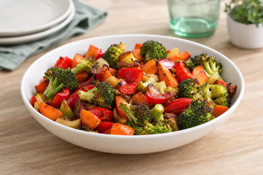 Roasted mixed vegetables with broccoli, carrots and peppers in a white bowl with a sprinkle of seasoning