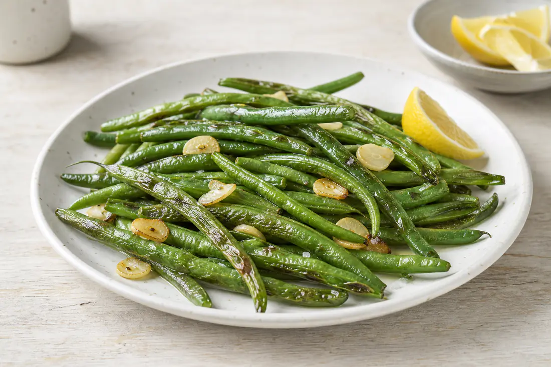 Blistered green beans with garlic and a squeeze of lemon on a white plate