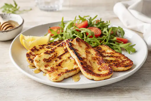 Golden browned halloumi slices on a white plate with lemon wedges, honey and a small salad