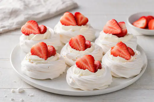 Small white meringue nests filled with whipped cream and strawberries on a white plate