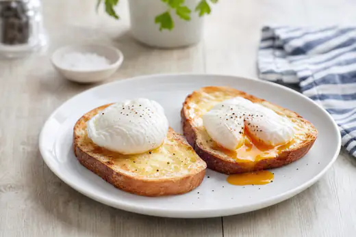 Two neat poached eggs on slices of buttered toast, one cut open with a runny yolk, on a white plate