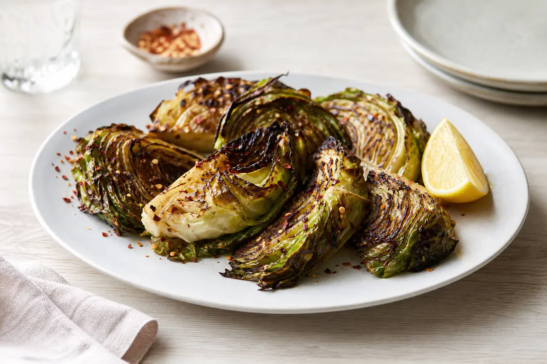 Charred hispi cabbage wedges with crisp dark edges, chilli flakes and lemon on a white serving plate