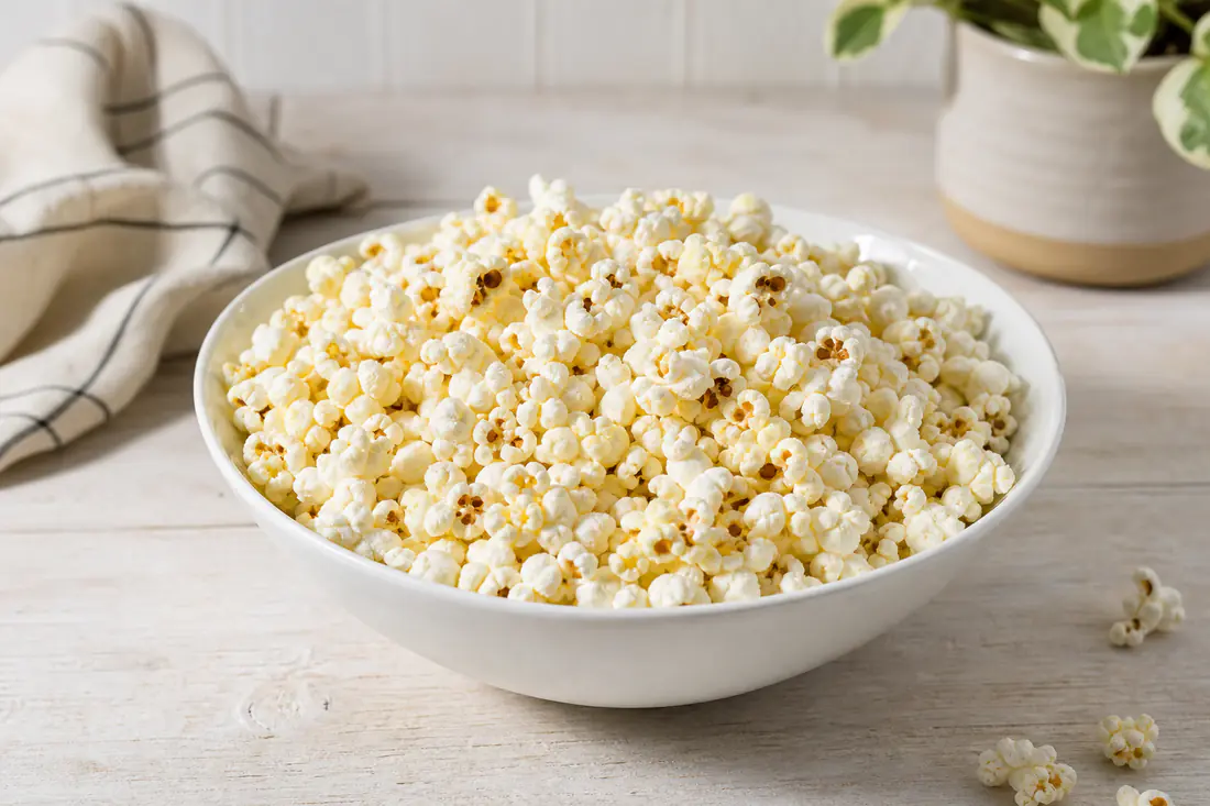 A white bowl of freshly popped, lightly salted popcorn on a kitchen worktop
