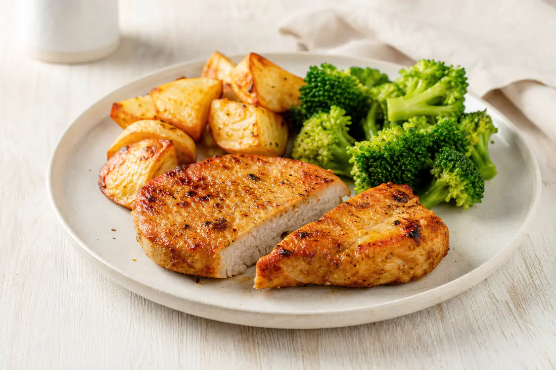 Two golden pork loin steaks cut open to show a juicy centre, served with roast potatoes and broccoli