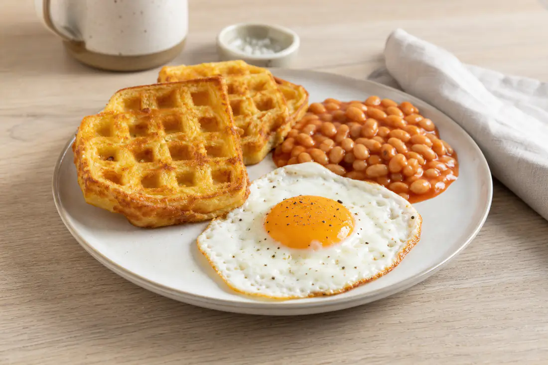 Three golden crispy potato waffles on a plate with a fried egg and baked beans