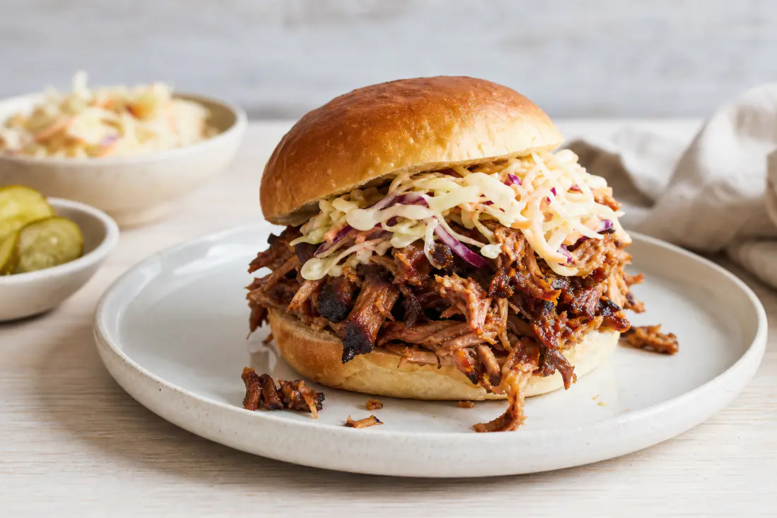 Shredded barbecue pulled pork piled in a soft bun with coleslaw, with crisp browned edges visible