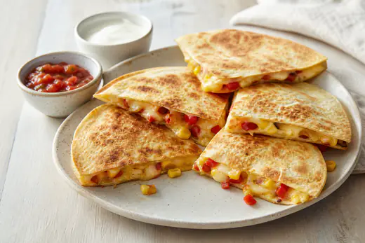 Golden half-moon cheese quesadillas cut into wedges on a board with soured cream and salsa