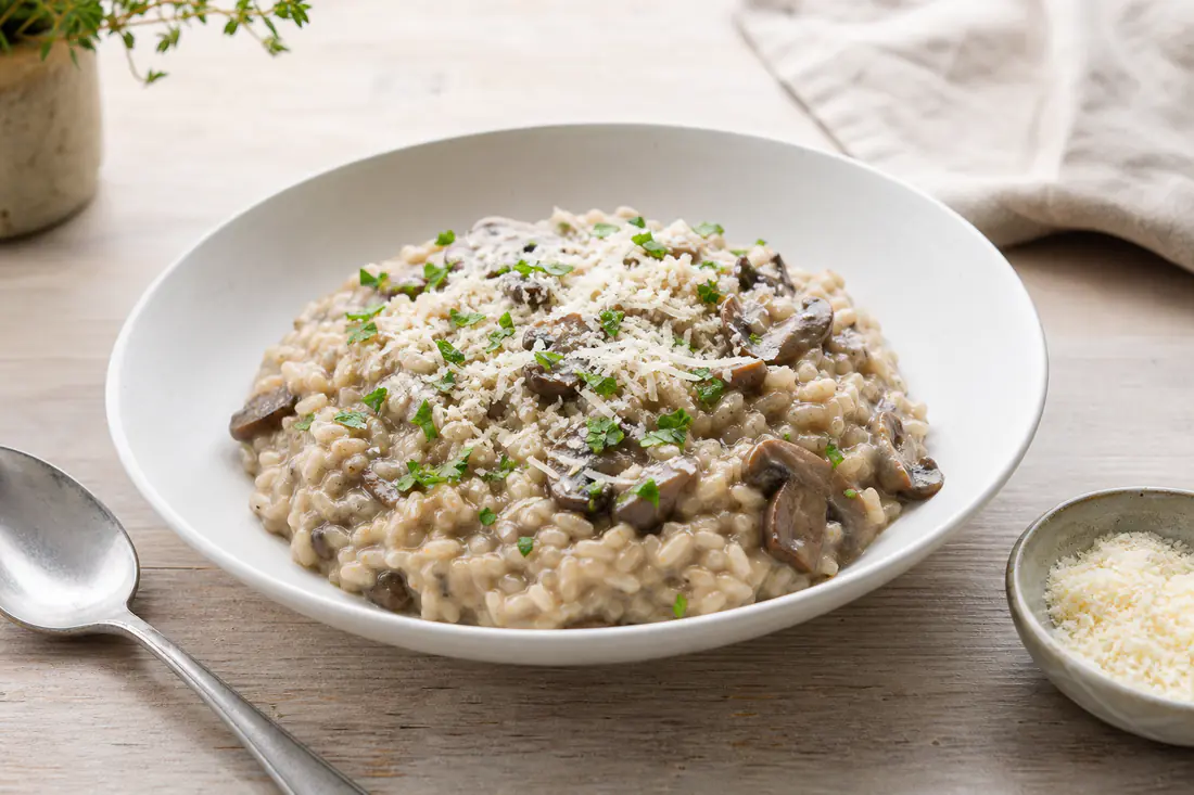 A shallow bowl of creamy mushroom risotto topped with grated parmesan and chopped parsley