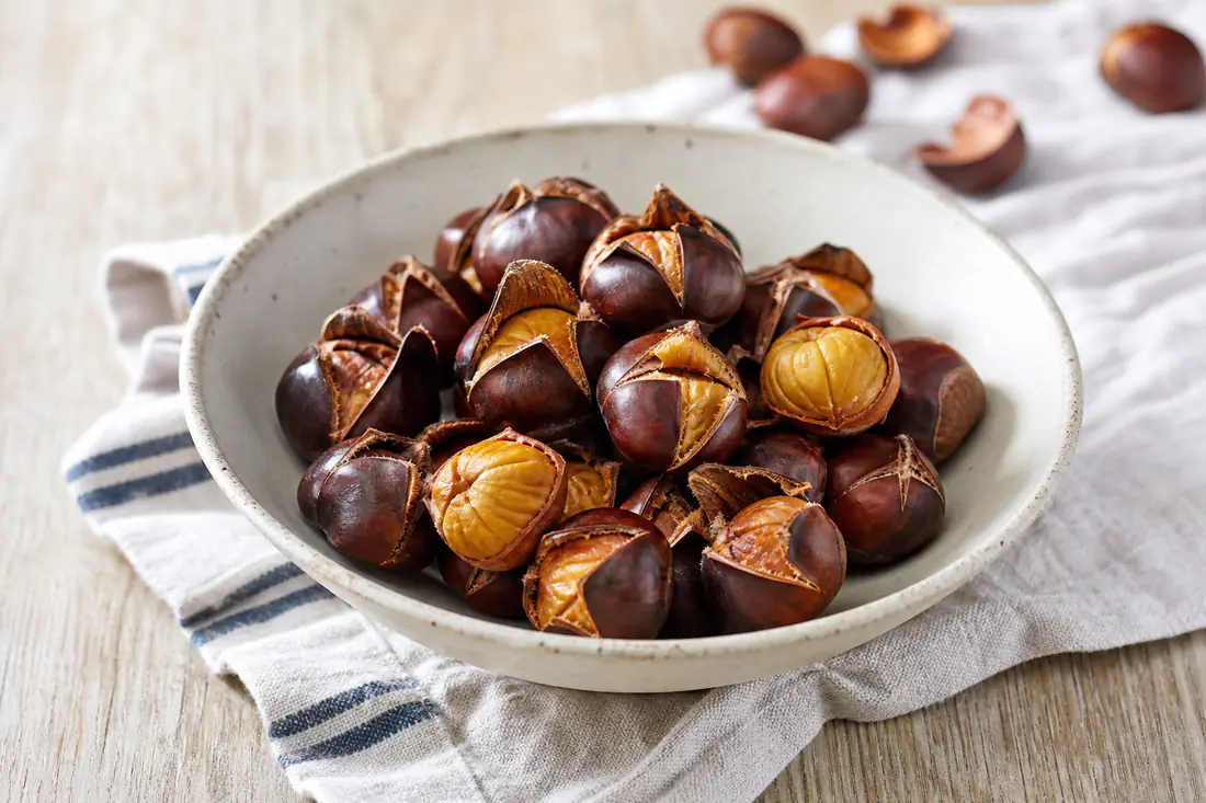 Freshly roasted chestnuts with split shells in a rustic bowl, some peeled to show the golden nut inside