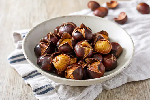 Freshly roasted chestnuts with split shells in a rustic bowl, some peeled to show the golden nut inside