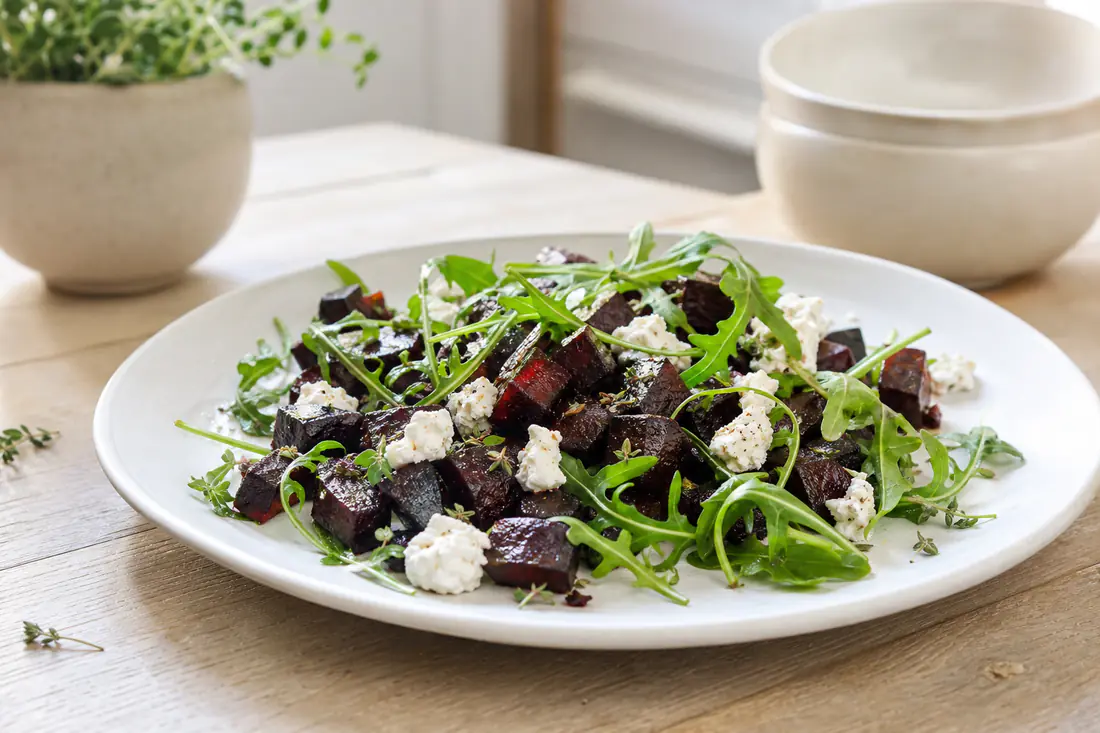 Deep purple roasted beetroot cubes with caramelised edges and thyme on a white plate with goat's cheese