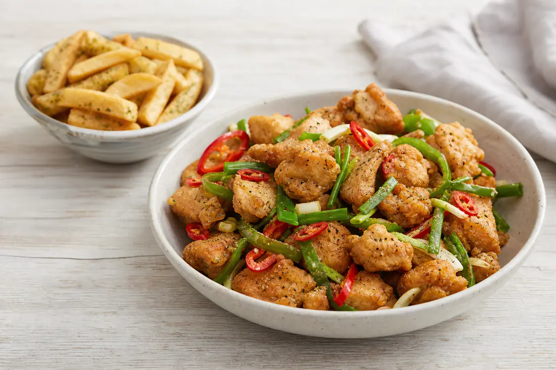 Crispy golden salt and pepper chicken pieces with sliced red chilli, green pepper and spring onion in a bowl