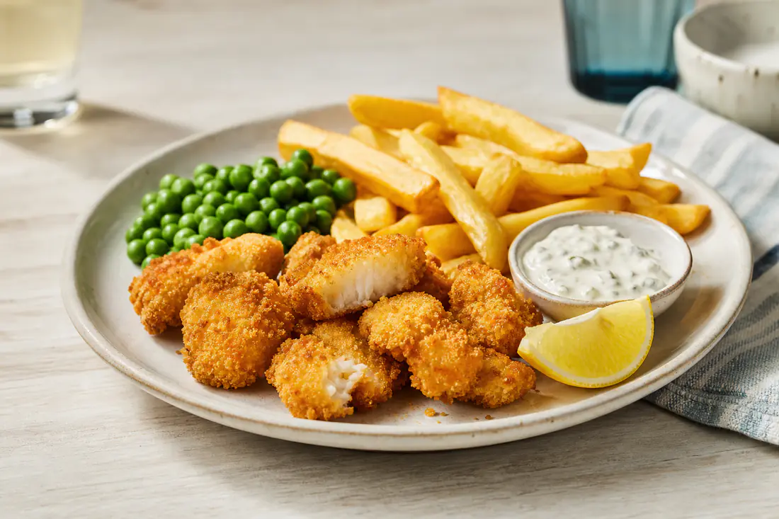 Golden breaded scampi with chips, peas and a lemon wedge on a plate with a small dish of tartare sauce