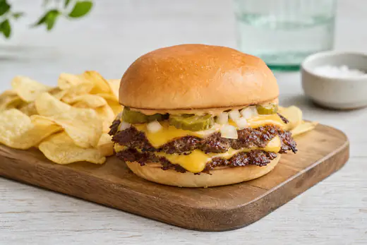 A double smash burger with melted cheese, pickles and onion in a soft bun on a wooden board